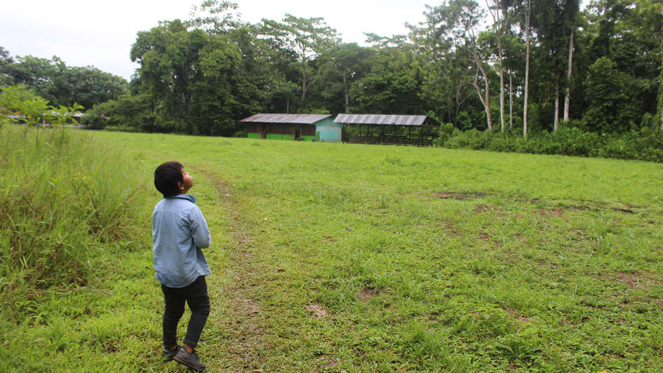 Ein Kind steht auf einer großen Wiese vor einem Haus, Peru 2022.