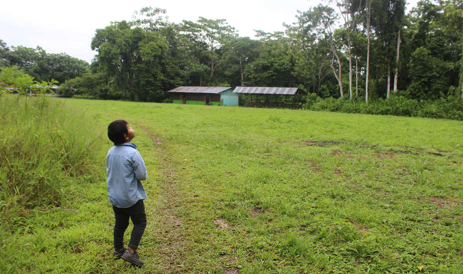 Ein Kind steht auf einer großen Wiese vor einem Haus, Peru 2022.