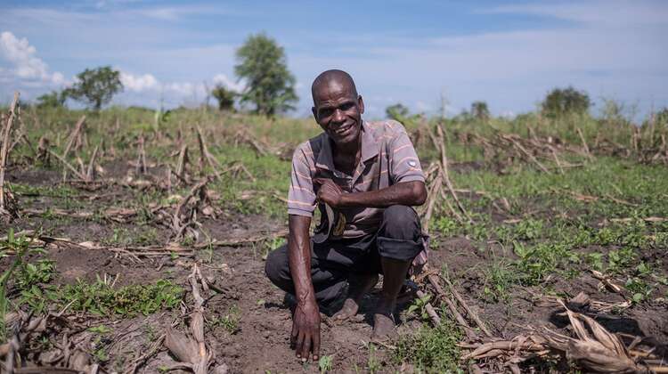 Ein Mann hockt auf einem Maisfeld und lächelt in die Kamera.