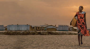 Im Vordergrund eine Frau mit einem gelben Kanister, im Hintergrund sieht man Zelte.