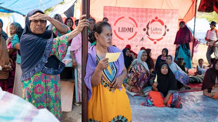 Frauen sitzen und stehen unter einem Zelt.