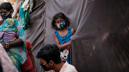 Ein Mädchen mit Mundschutz steht an einem Zelt aus schwarzen Planen.