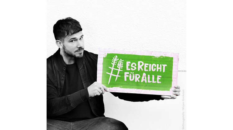 Sänger und Songwriter Robert Redweik hält ein Schild mit dem Welthungerhilfe-Hashtag #EsReichtFürAlle.