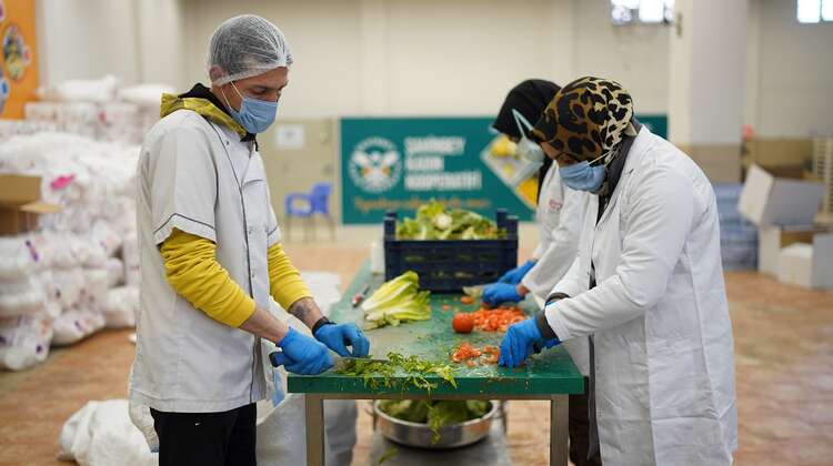 Drei Personen stehen um einen Tisch, auf dem sie eine große Menge Gemüse für die weitere Zubereitung von Mahlzeiten schneiden
