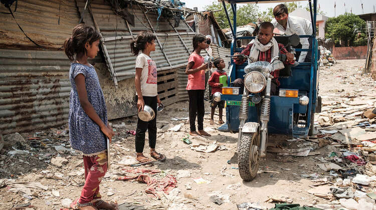 Kinder gehen mit leeren Schüsseln auf ein Riksha zu.