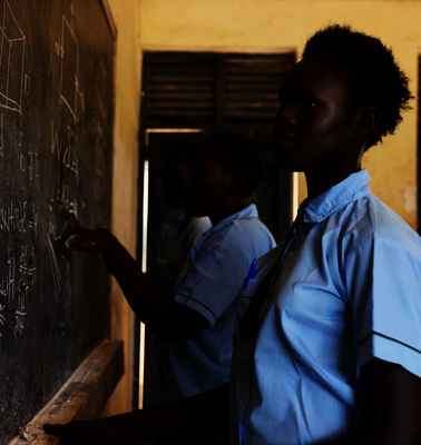 Bild aus einem Projekt im Südsudan mit Schulspeisungen, ein Mädchen steht an einer Schultafel.