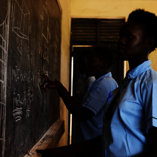 Bild aus einem Projekt im Südsudan mit Schulspeisungen, ein Mädchen steht an einer Schultafel.