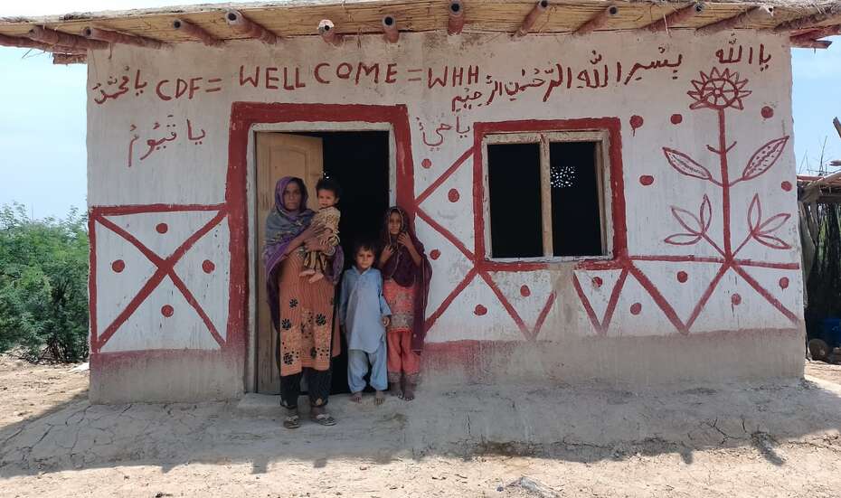 Eine Familie steht in der Tür eines von Hand bemalten kleinen Hauses.