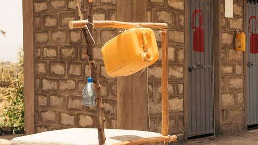 Im Vordergrund sieht man einen Brunnen, im Hintergrund ein Gebäude mit mehreren Türen.