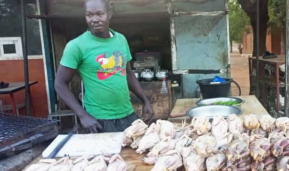 Ein Mann steht an einem Tisch, vor ihm liegen viele gerupfte Hühner.