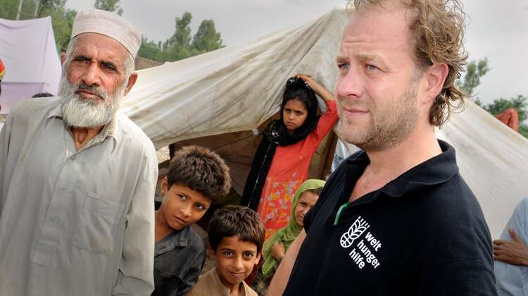 Ein Mann in schwarzem Welthungerhilfe-Tshirt vor einem Zelt.