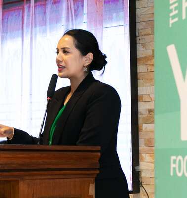 Eine Frau hinter einem Rednerpult spricht in ein Mikrophon.