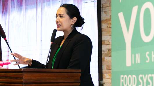 Eine Frau hinter einem Rednerpult spricht in ein Mikrophon.