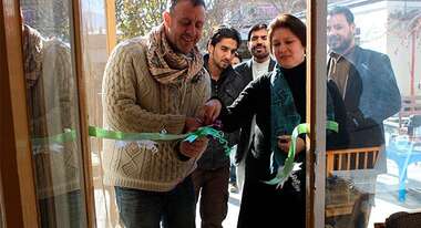 Welthungerhilfe-Mitarbeiter schneiden eine Scherpe vor einem Eingang feierlich durch.