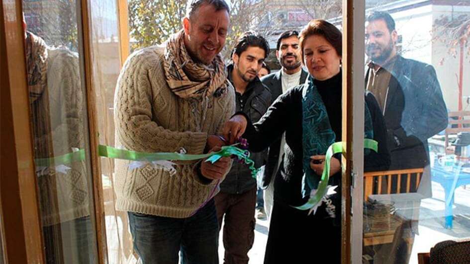 Welthungerhilfe-Mitarbeiter schneiden eine Scherpe vor einem Eingang feierlich durch.