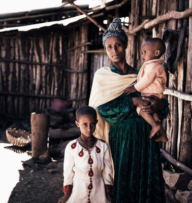 Eine Frau steht mit ihren beiden Kindern vor einer Holzhütte, Äthiopien.