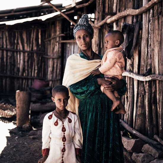 Eine Frau steht mit ihren beiden Kindern vor einer Holzhütte, Äthiopien.