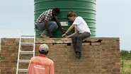 Farmer Innocent Chifamba, Rodney Mushongachiware von APT und Anne-Catrin Hummel von der Welthungerhilfe schließen gemeinsam den neuen Wassertank an.