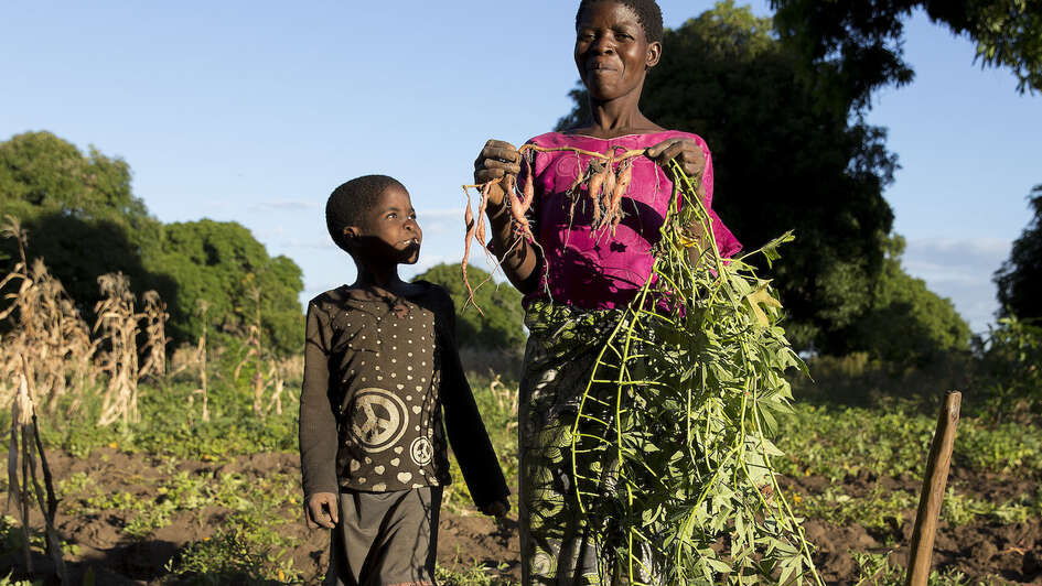 Eine Frau und ein Kind stehen auf einem Feld. Die Frau hält stolz eine Rübe in die Luft.