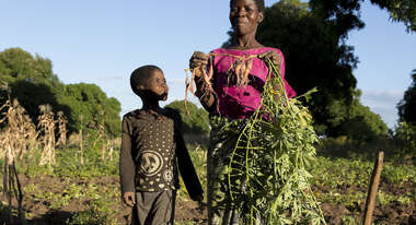 Eine Frau und ein Kind stehen auf einem Feld. Die Frau hält stolz eine Rübe in die Luft.