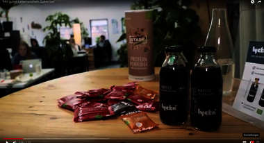 zwei Flaschen Lycka Kaffe stehen auf einem Holztisch. Im Hintergrund ist ein Café zu sehen.