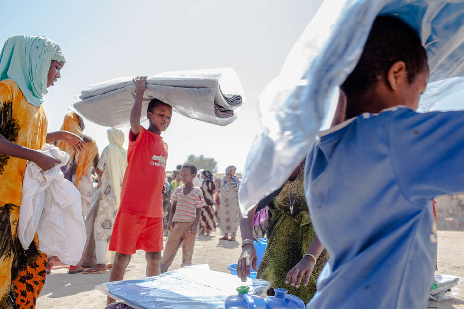 Kinder in einem Flüchtlingscamp werden bei einer Verteilung mit Decken und Kanistern versorgt