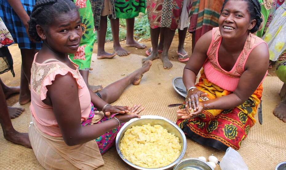 Zwei Frauen sitzen mit einer Schüssel voller Teig auf dem Boden und bereiten Essen zu.