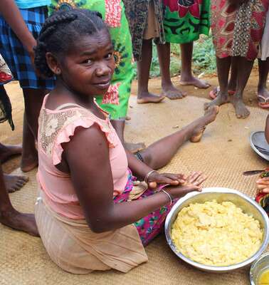 Zwei Frauen sitzen mit einer Schüssel voller Teig auf dem Boden und bereiten Essen zu.