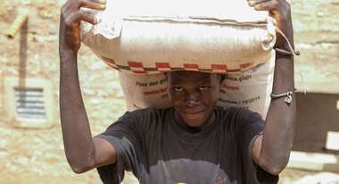Ein Mann bei einer Nahrungsmittelverteilung hält einen großen Sack auf Kopf und Schultern. 
